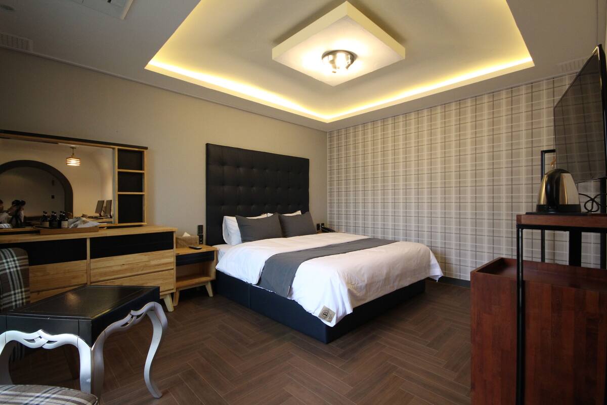 A modern bedroom with a large bed, a wooden dresser, a desk, and a chair.