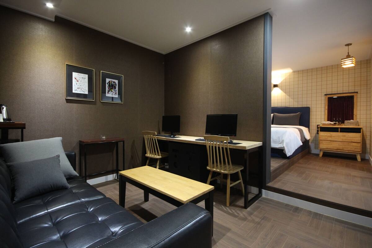 A modern hotel room with a sofa, desk, chairs, a bed, and a dresser.