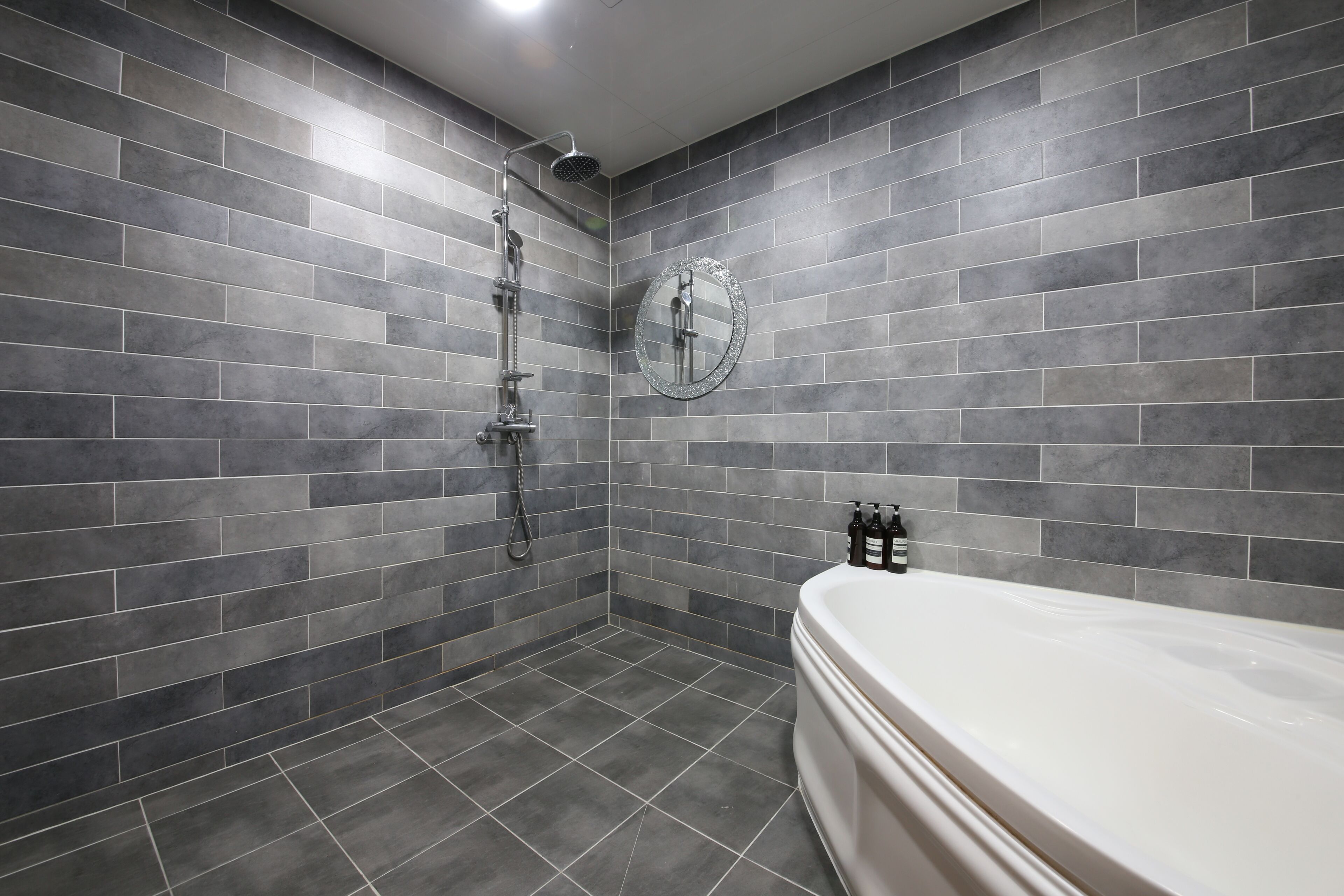 Un baño moderno con azulejos grises, una bañera independiente y un cabezal de ducha de mano.
