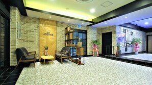 A reception area with a brick wall, wooden panel, and a black-framed shelf with decorative items. There are two chairs and a small table with a vase. - Instar Hotel Yangsan (Yangsan)