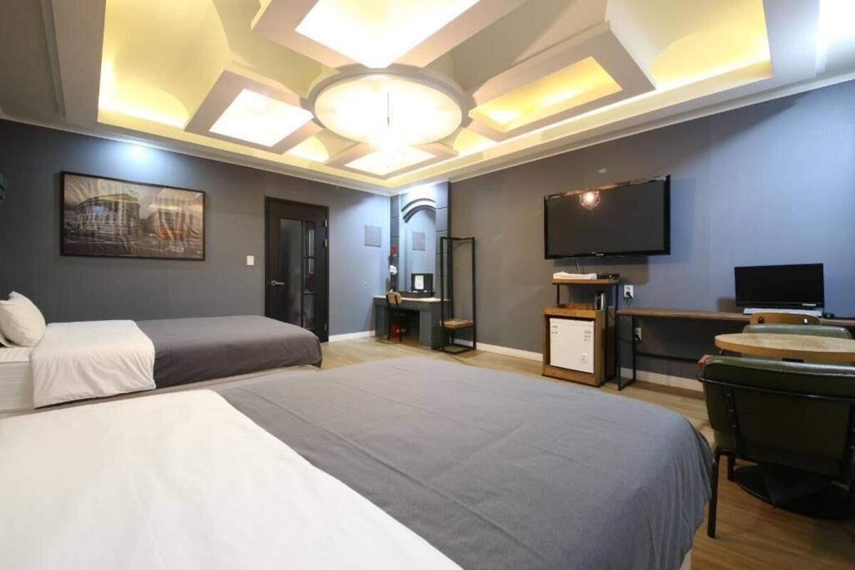 A hotel room with two beds, a desk, a TV, and a ceiling light fixture.