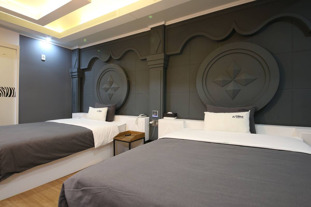 A hotel room with two beds, each with a grey bedspread and white pillows. There is a small wooden table between the beds.