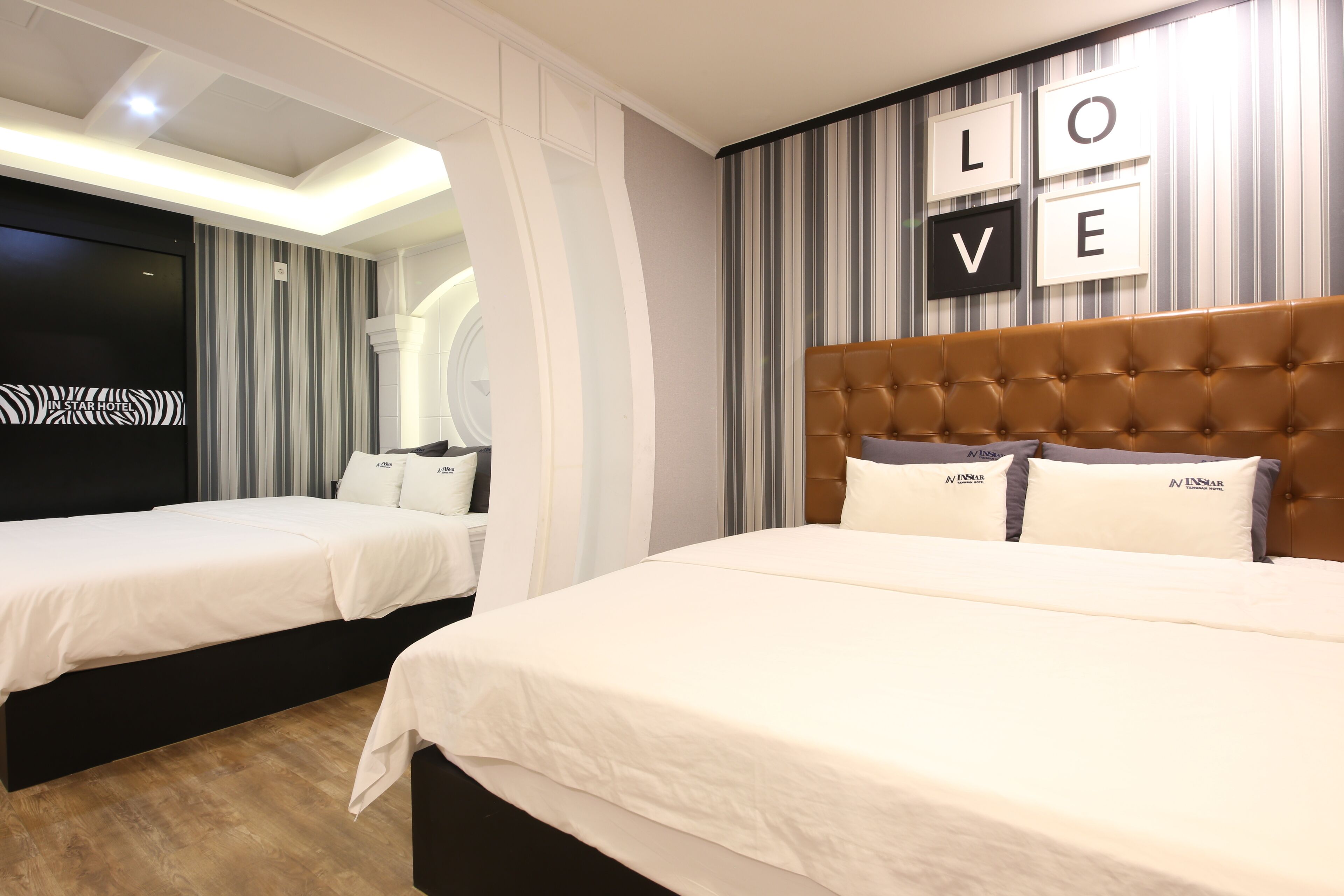 A hotel room with two beds, a large tufted headboard, and a 'LOVE' sign on the wall.
