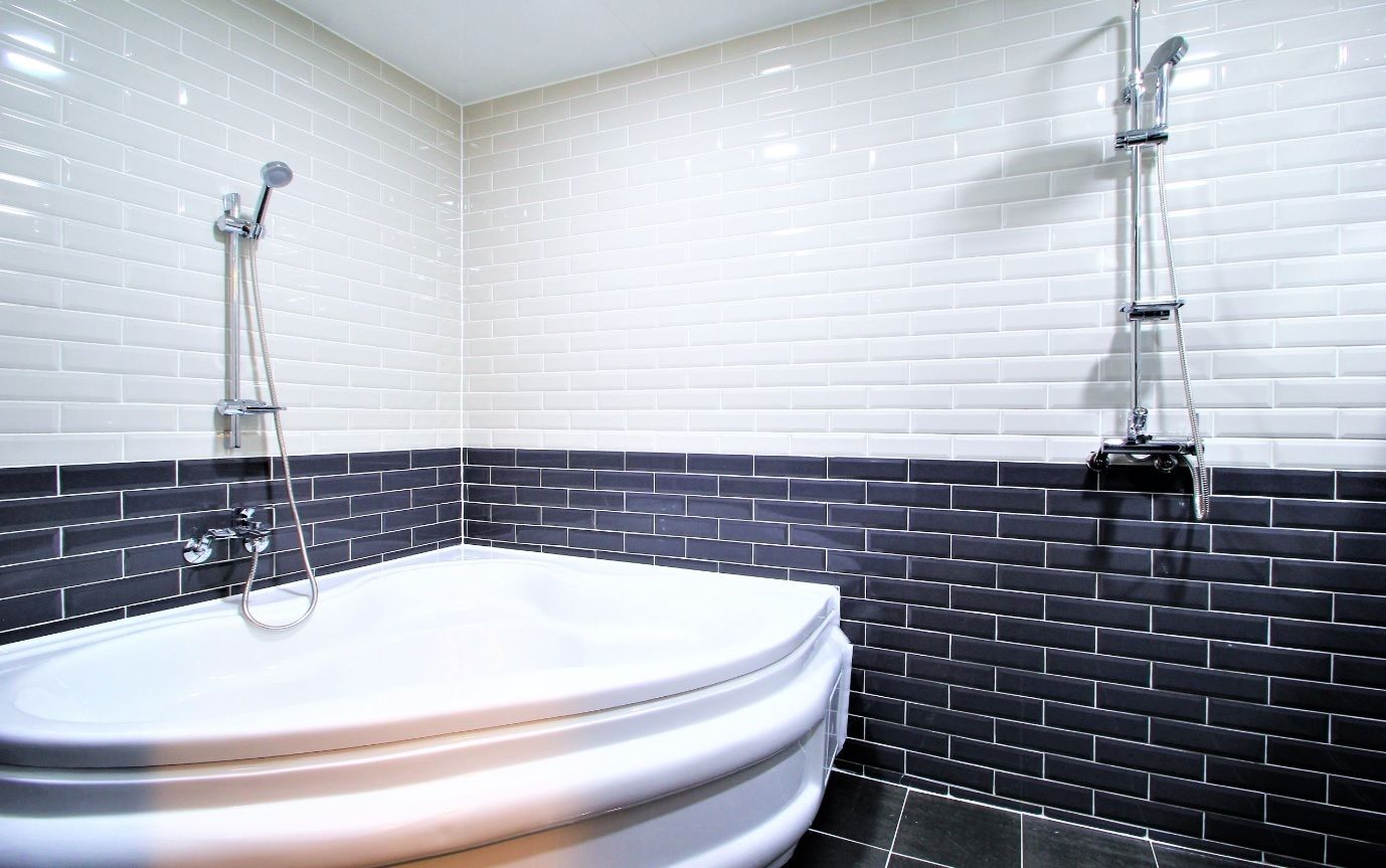 Une salle de bain avec une baignoire blanche, des murs recouverts de carreaux noirs et une pomme de douche chromée.