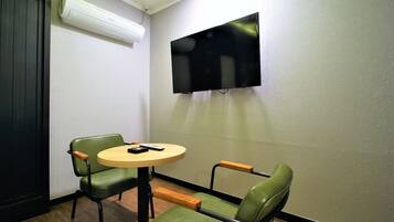 Una habitación pequeña con una sola silla verde, una mesa redonda y un televisor de pantalla plana montado en la pared.