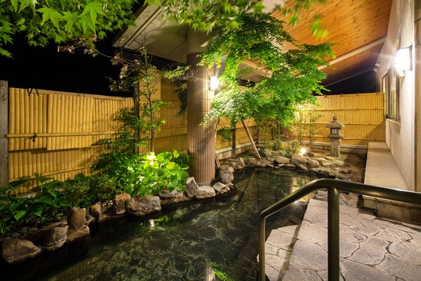 Un jardin japonais traditionnel avec un bassin à carpes koï, une clôture en bambou et des lanternes en pierre.