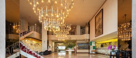 Un vestíbulo espacioso con una imponente araña de cristal, una escalera y una mesa de recepción.