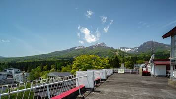 Una terraza en la azotea con vistas a una cadena montañosa, un edificio de tejados rojos y una valla blanca.