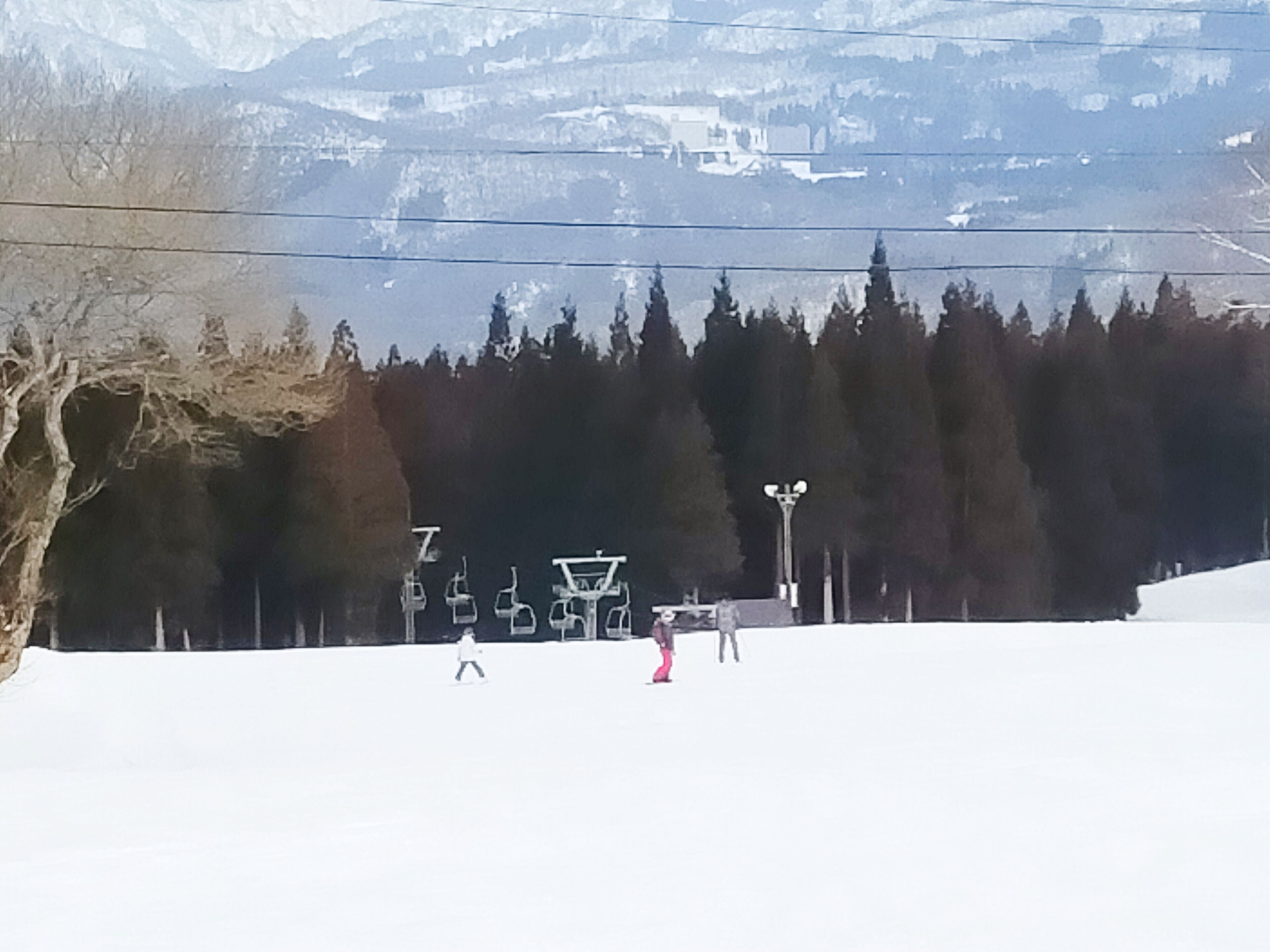 A ski slope with a chairlift, trees, and a mountain backdrop.