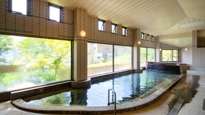 En stor indendørs swimmingpool med glasvægge, flisegulv og træloft.