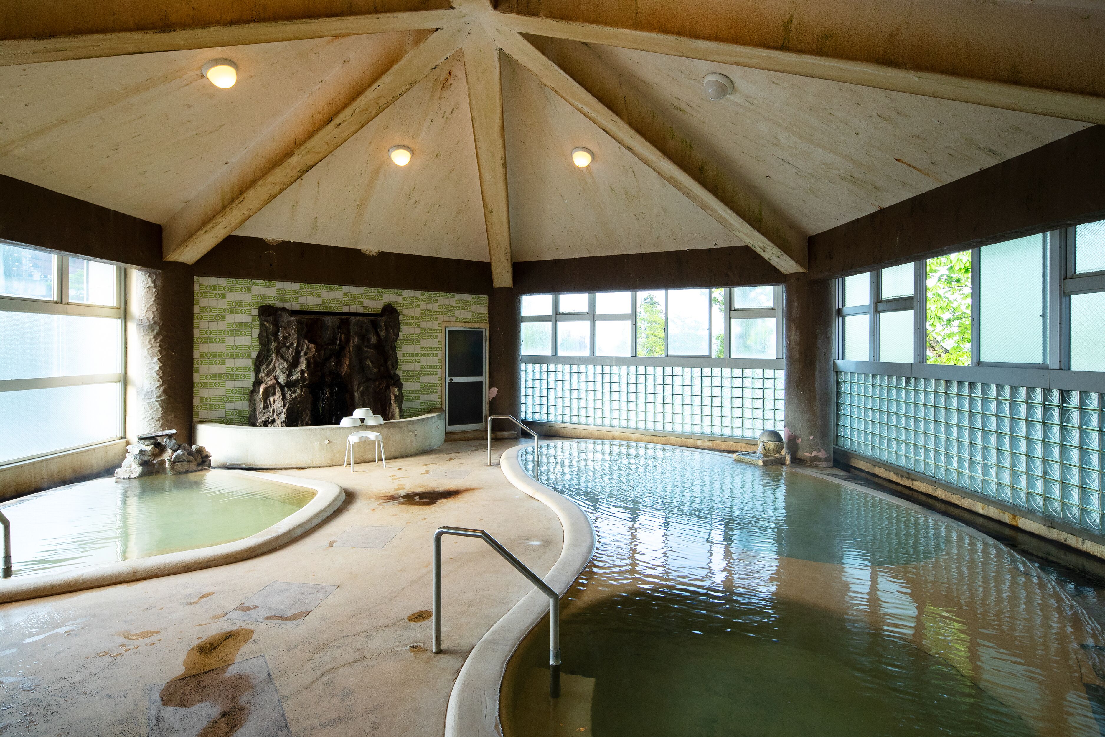 Piscina interior con techos altos, pared de piedra y vistas a zonas verdes.