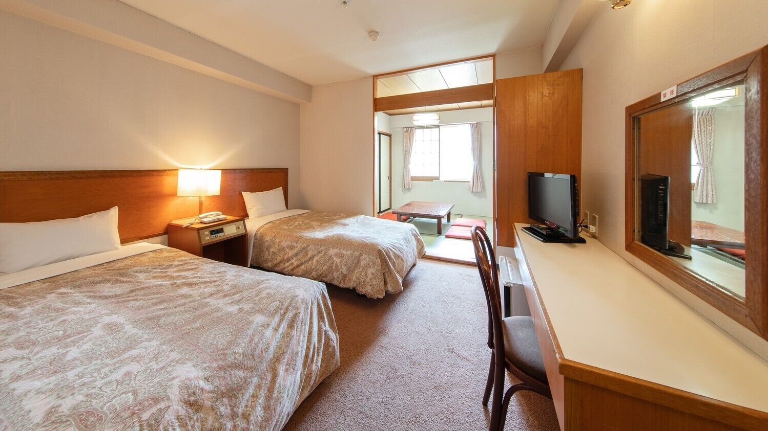Une chambre d’hôtel avec deux lits, un bureau avec une télévision et une vue sur l’extérieur.