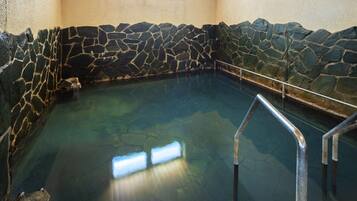 Una piscina techada con paredes de piedra, agua cristalina, barandillas de metal y un ventanal.
