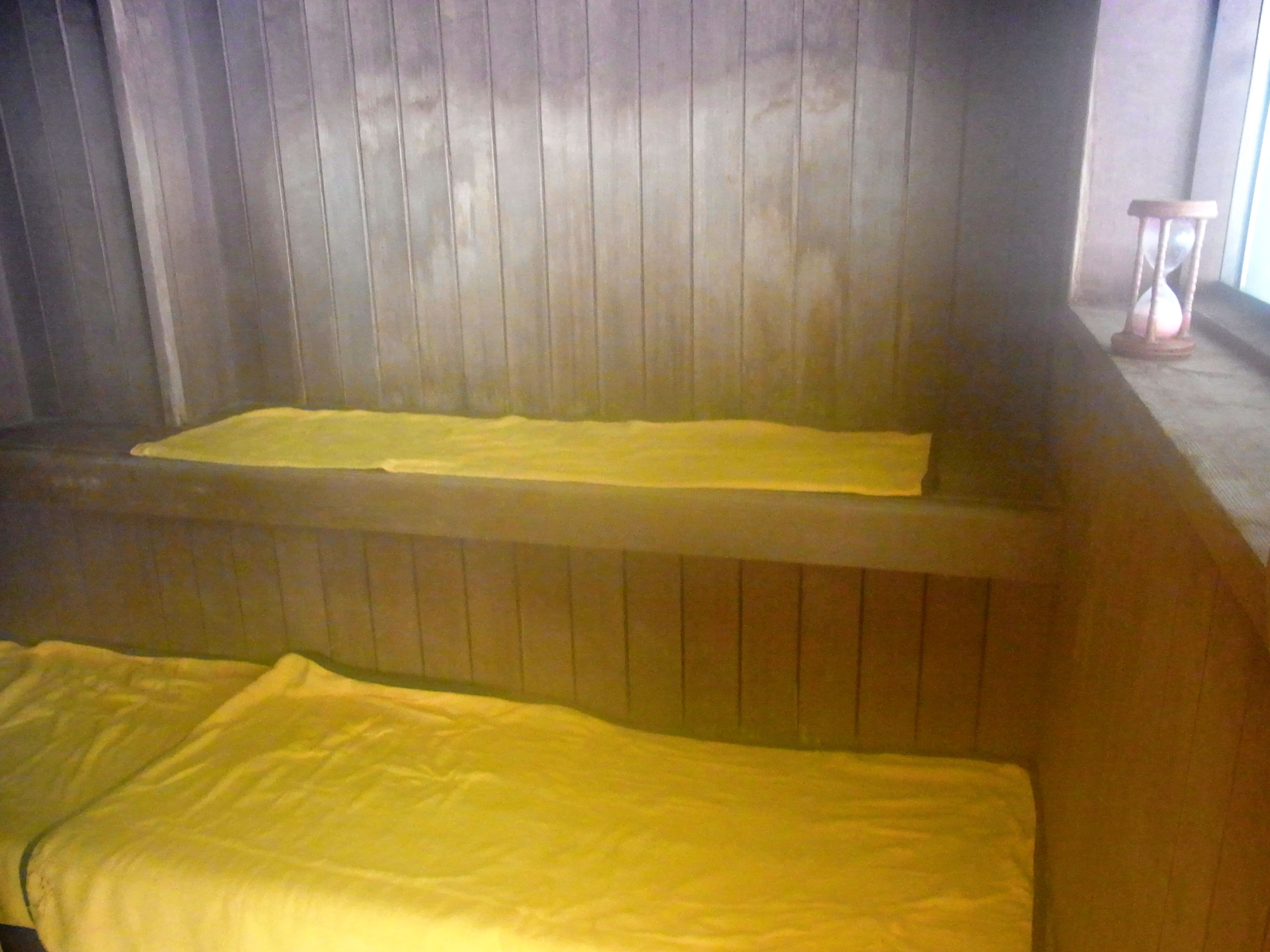 Une pièce avec un banc en bois et un lit recouvert d’une couverture jaune.