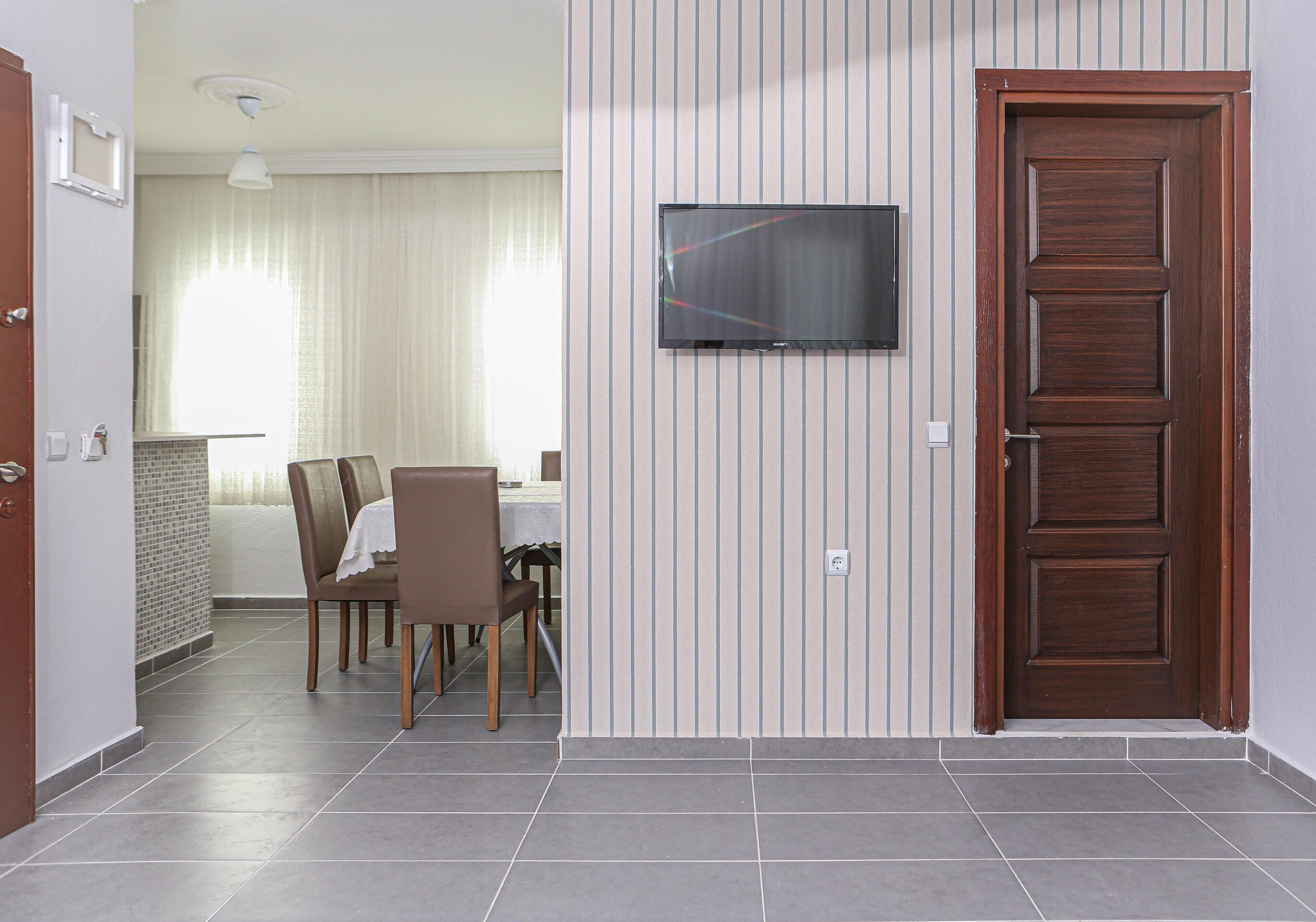 A dining area with a table and chairs, a television mounted on the wall, and a wooden door.