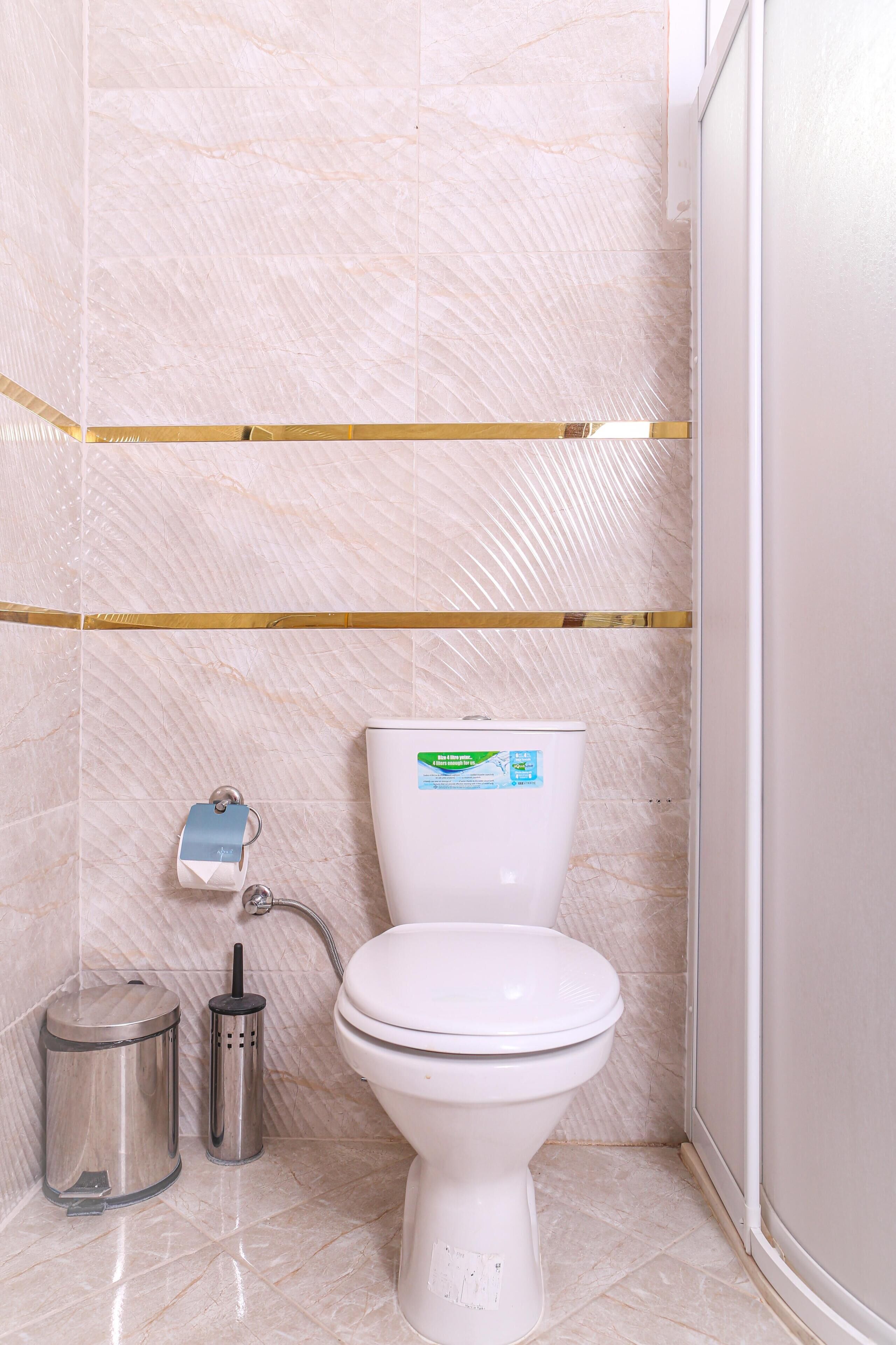 A bathroom with a toilet, a trash bin, and a toilet brush.