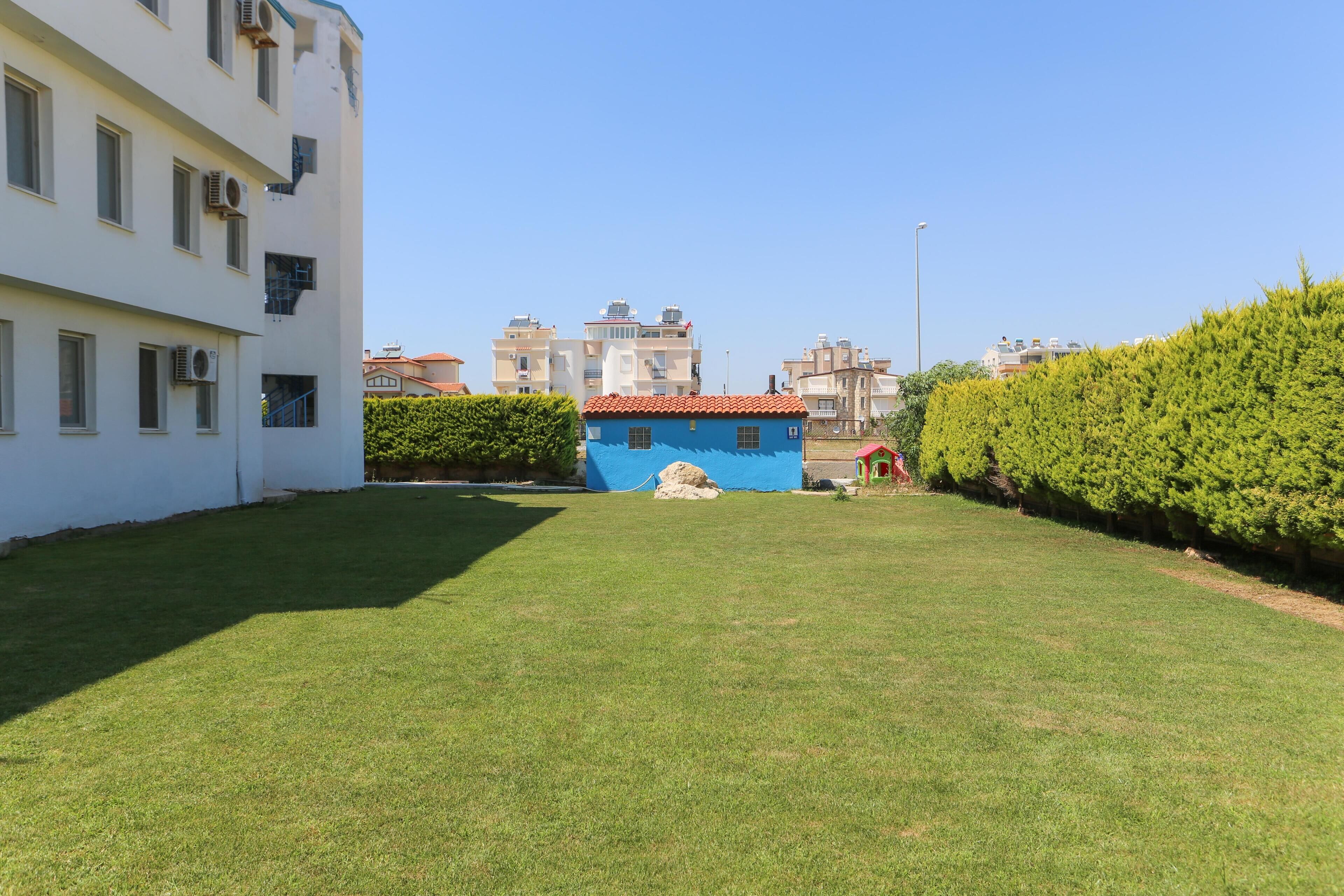 A courtyard with a well-maintained lawn, a blue building with a red roof, and a white building with multiple windows and air conditioning units.