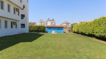 A courtyard with a well-maintained lawn, a blue building with a red roof, and a white building with multiple windows and air conditioning units.