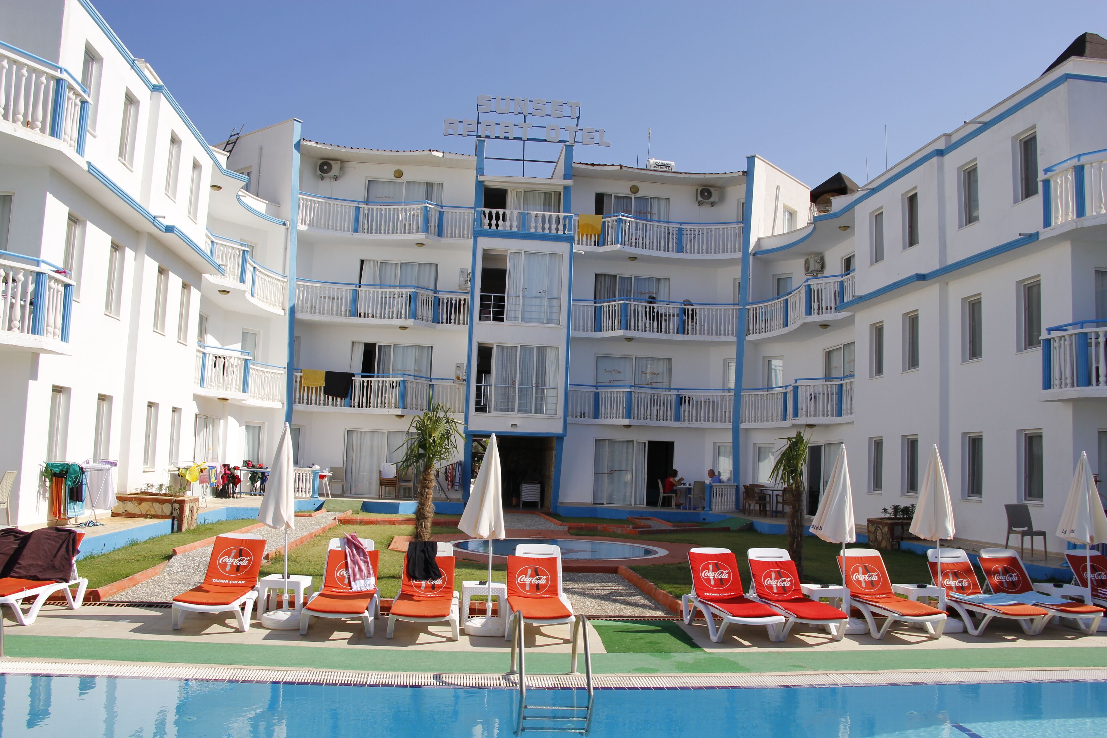A resort hotel with multiple balconies, a swimming pool, and lounge chairs with umbrellas.