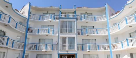 Un hotel de varios pisos con balcones, una entrada principal y zonas de estar al aire libre.