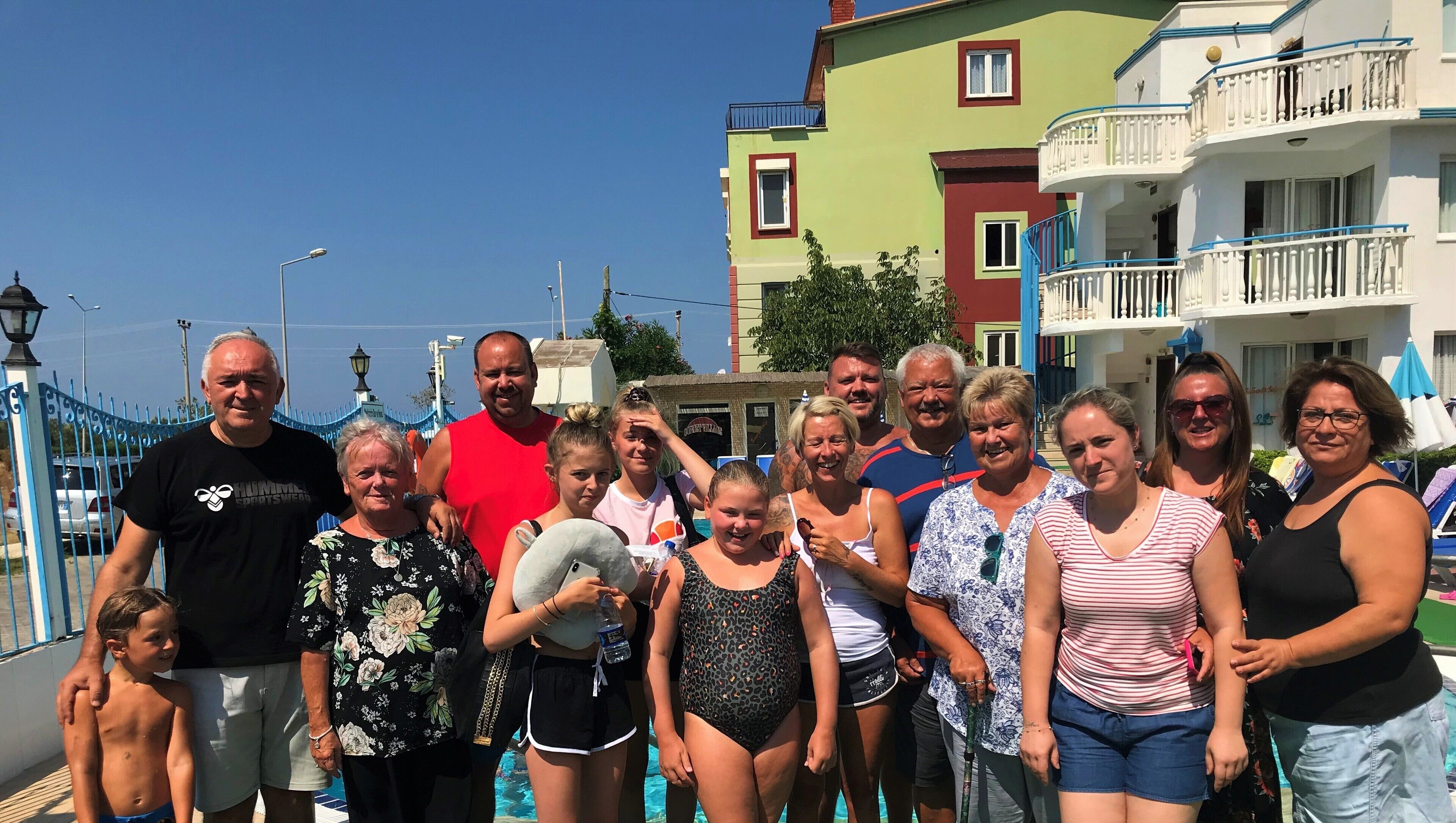 Um grupo de pessoas posando perto de uma piscina, com um edifício ao fundo.
