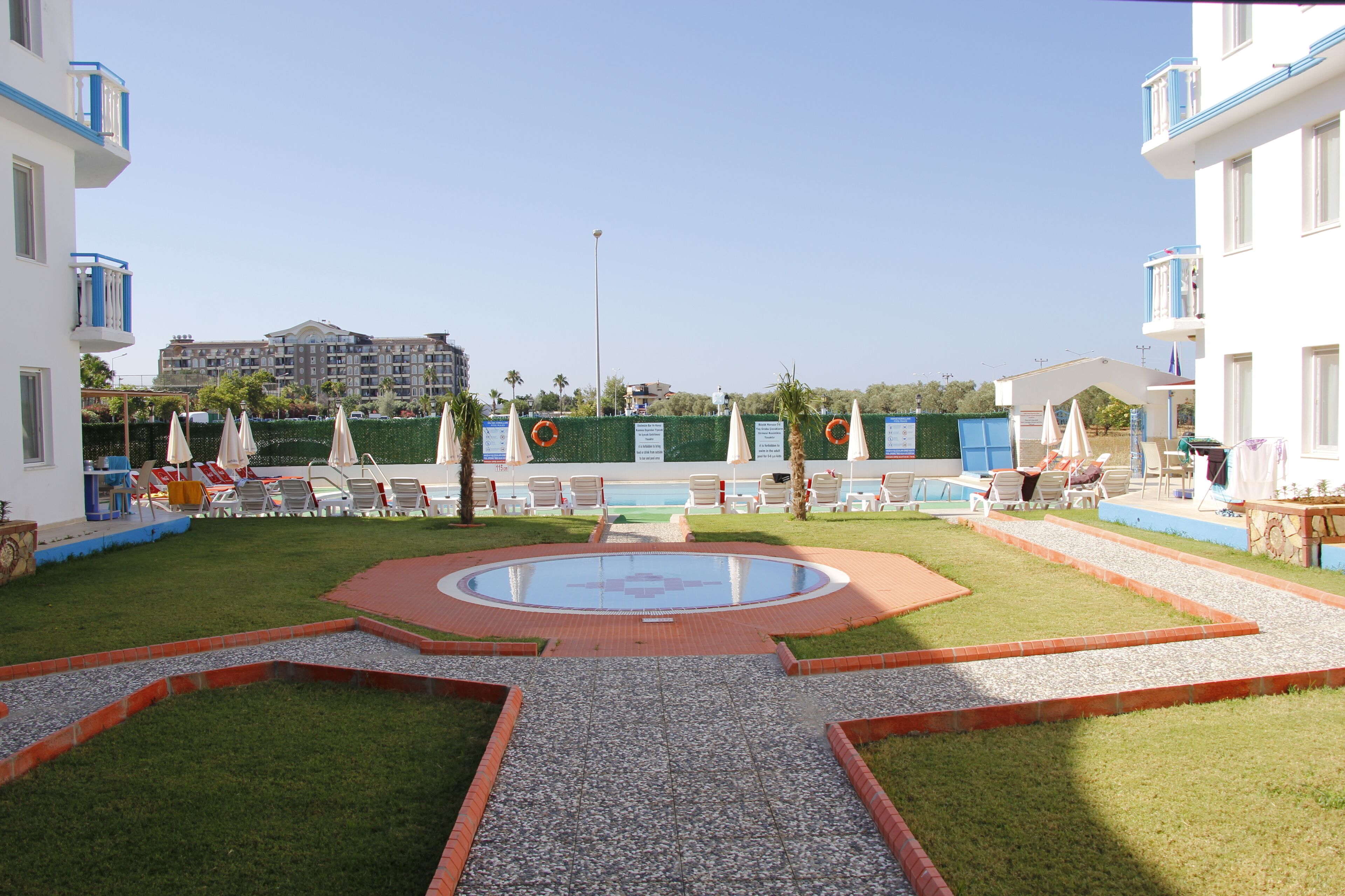 A pool area with lounge chairs and umbrellas, surrounded by a low brick wall and greenery.