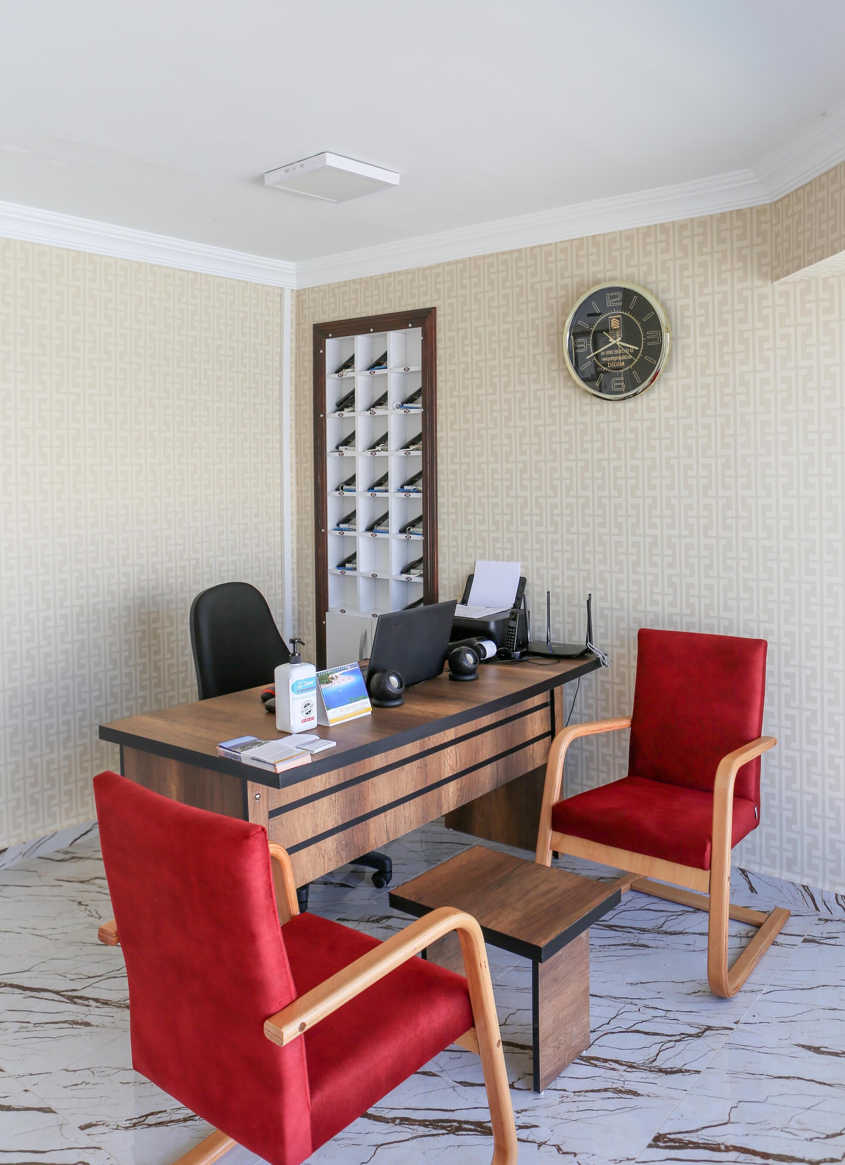A modern office with a wooden desk, two red chairs, a clock, and a wall-mounted shelf.