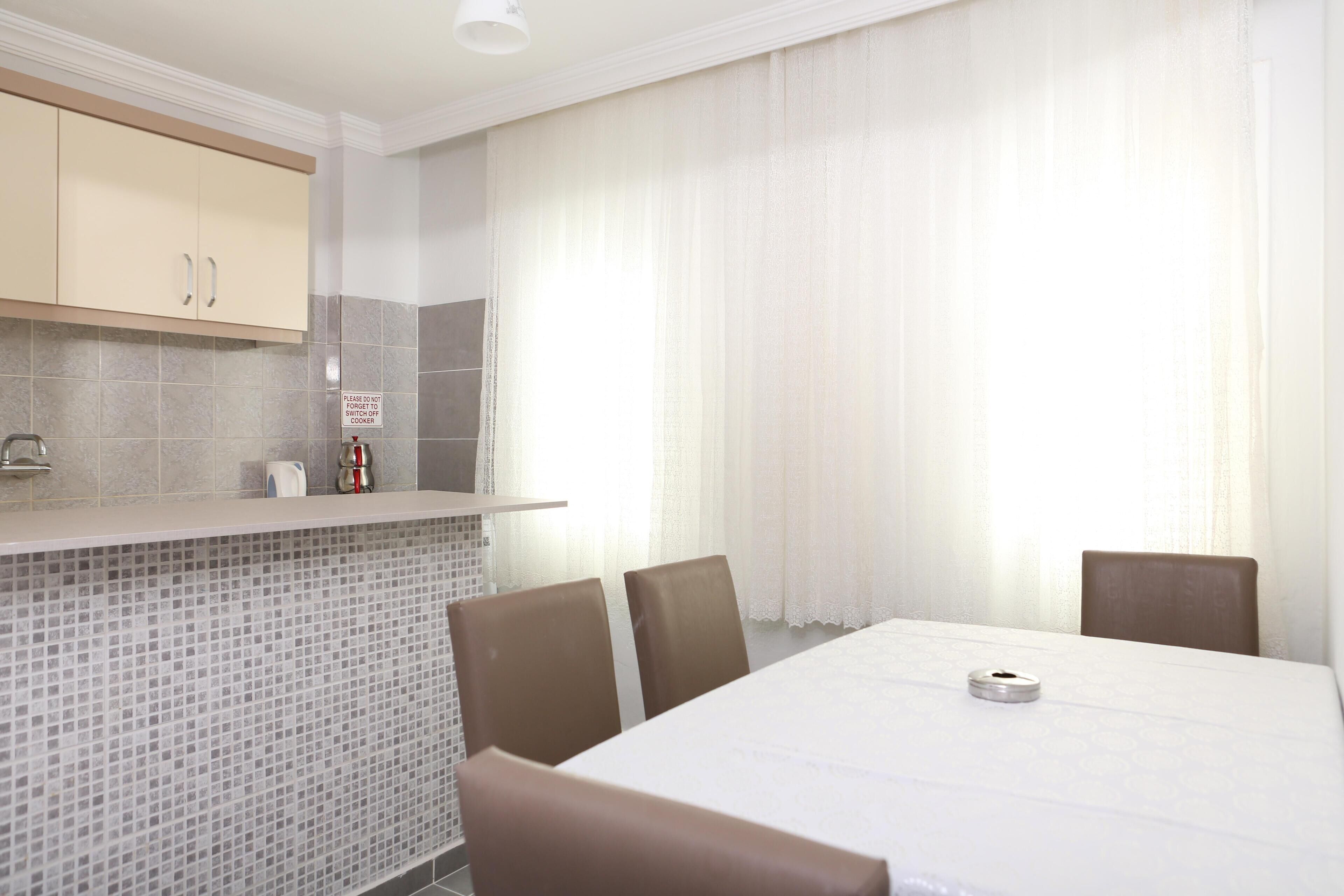 A modern kitchen with a tiled backsplash, a built-in oven, and a dining area with a table and chairs.
