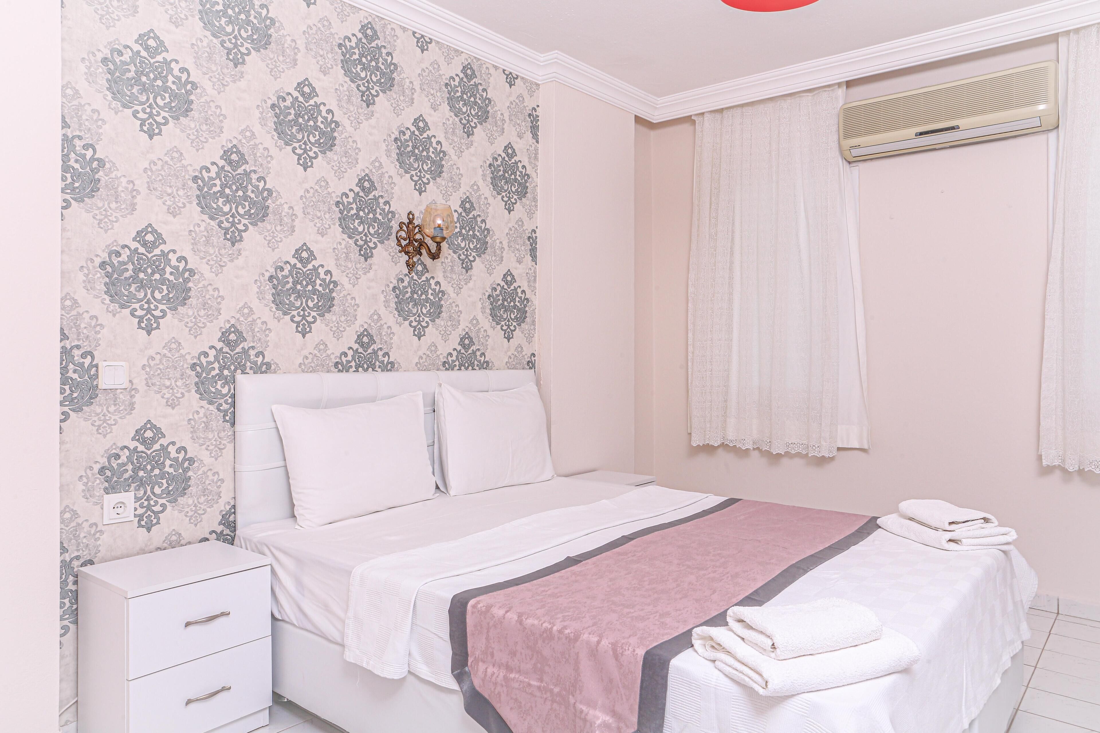 A bedroom with a bed, a nightstand, a wall-mounted air conditioner, and patterned wallpaper.
