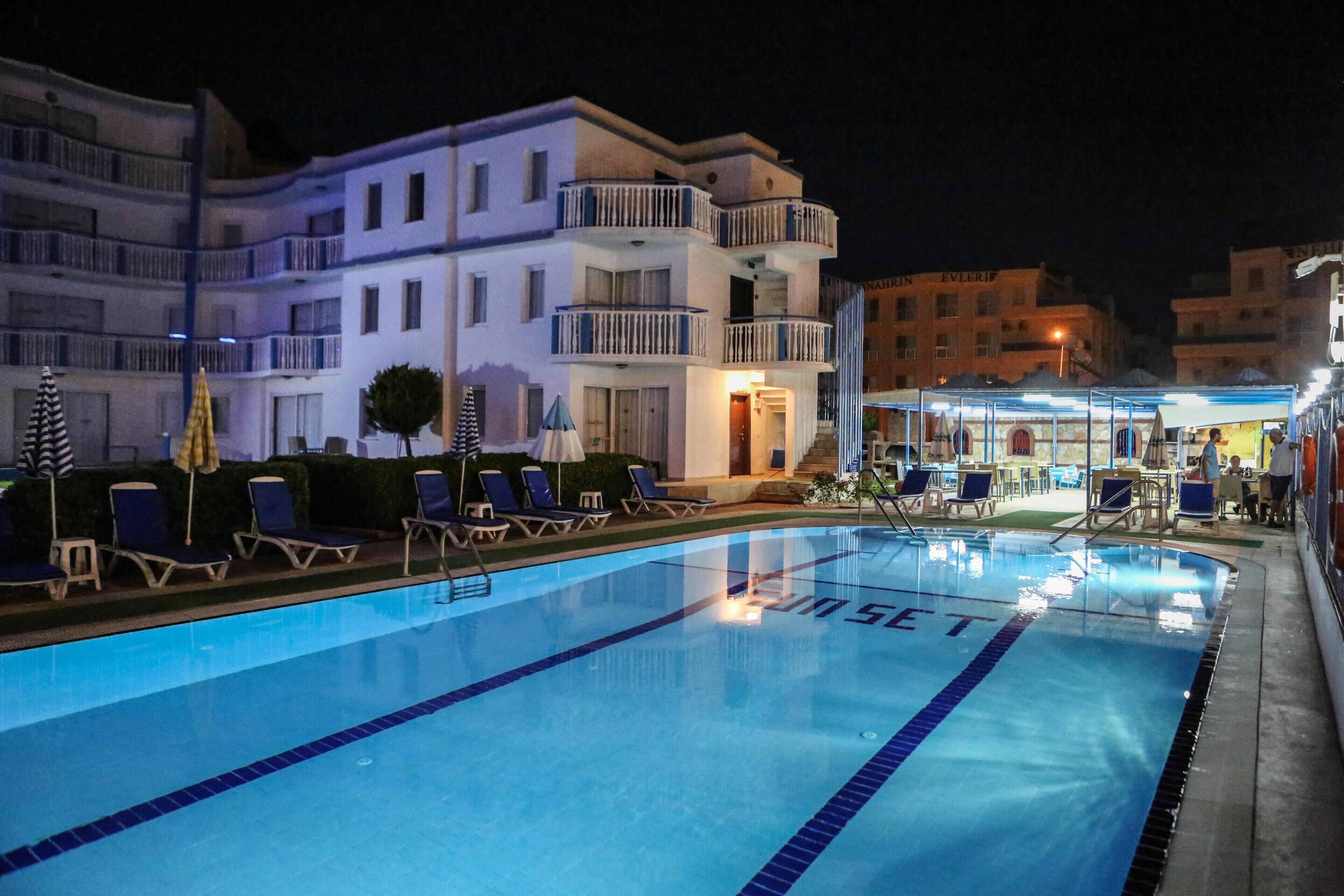 A swimming pool with lounge chairs and umbrellas, surrounded by buildings with balconies and outdoor seating areas.