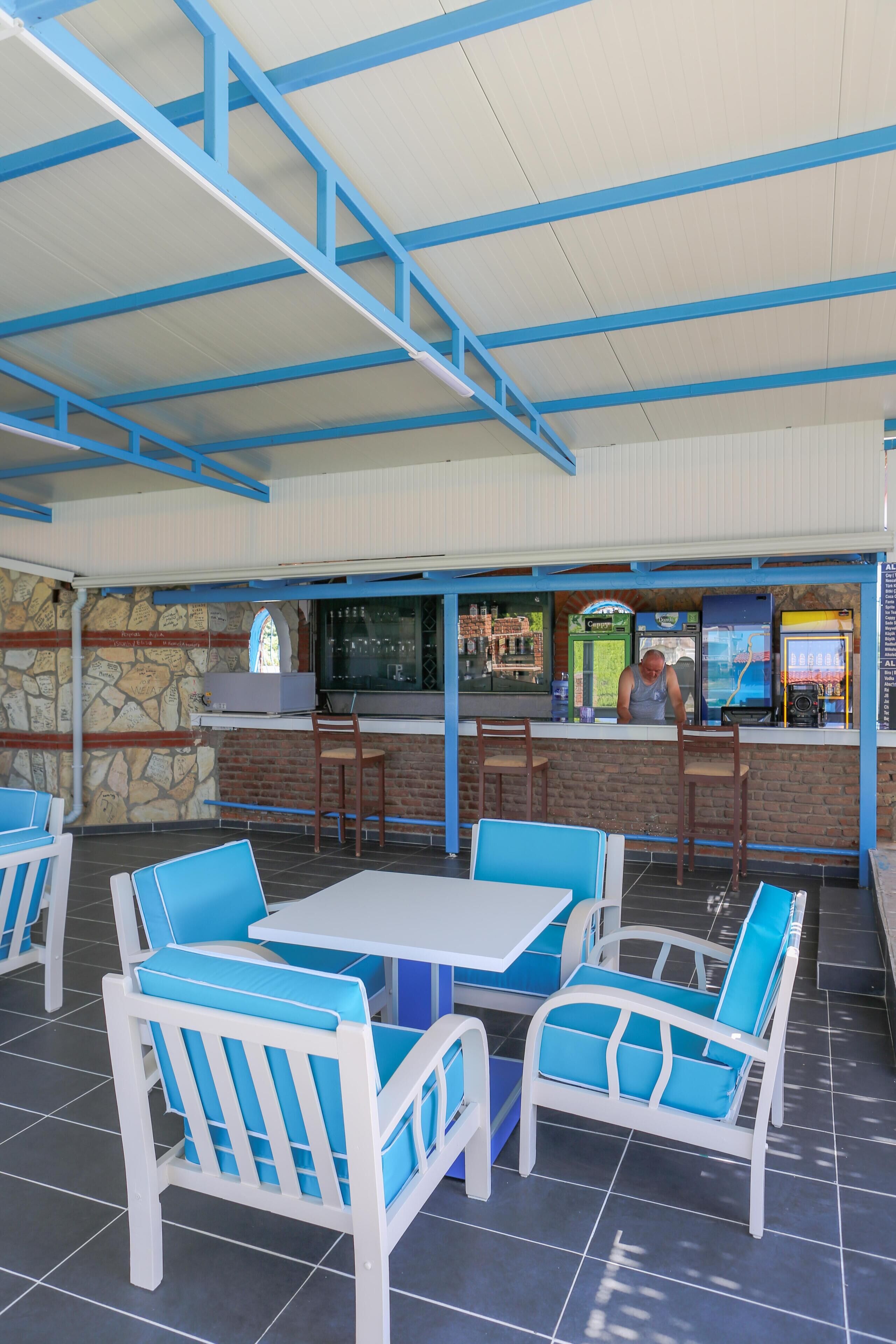 An outdoor café with blue and white furniture, a stone wall, and a bar area with a person behind the counter.
