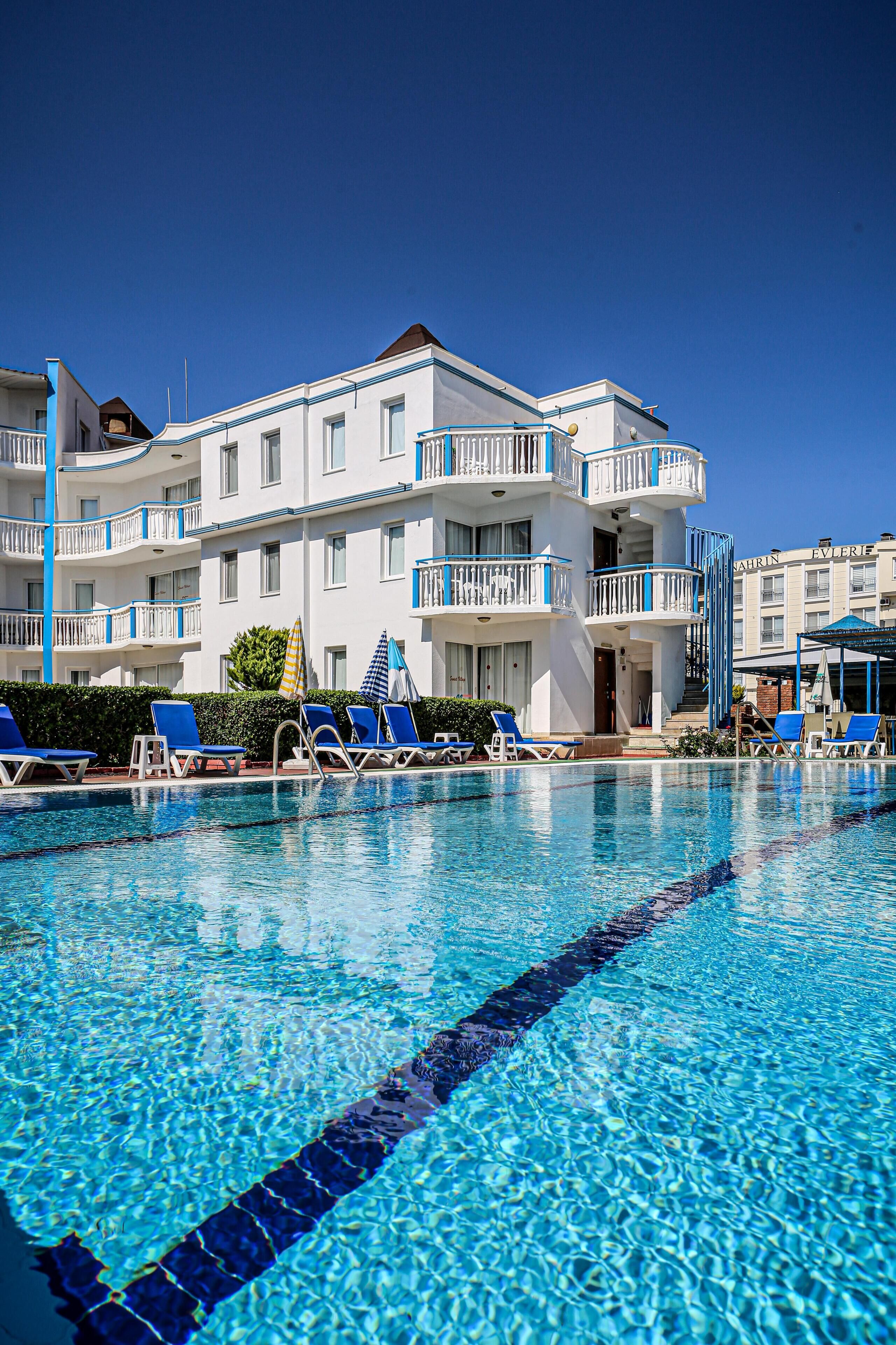 Una piscina con sillas reclinables azules y un edificio con balcones al fondo.