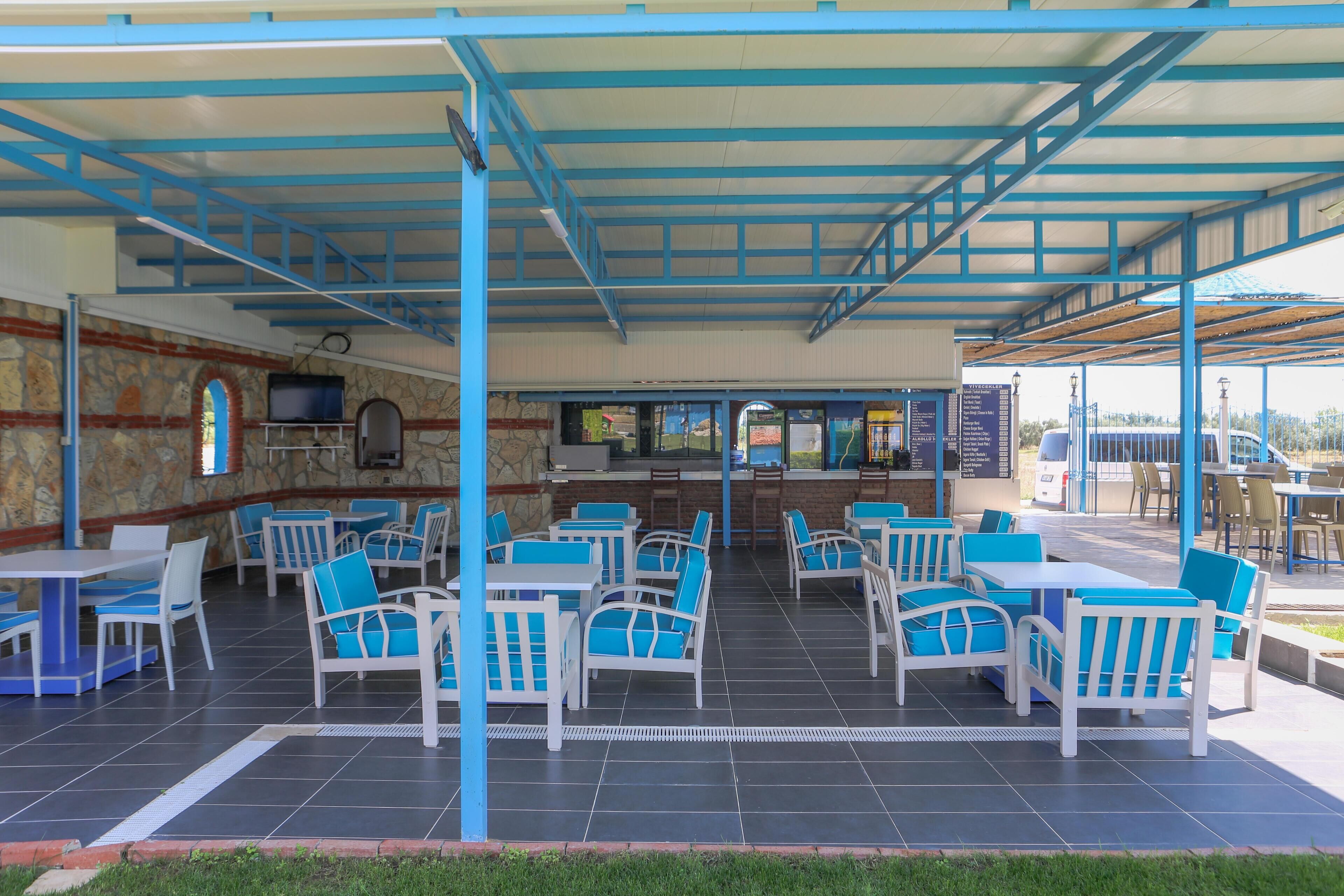 An outdoor cafe with blue and white furniture, a stone wall, and a covered area with a staircase.
