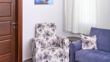 A living room with a wooden door, a patterned armchair, a blue sofa, a ceiling light, and a window with curtains.