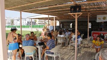 An outdoor patio area with tables and chairs, a covered roof, and a view of buildings in the background.
