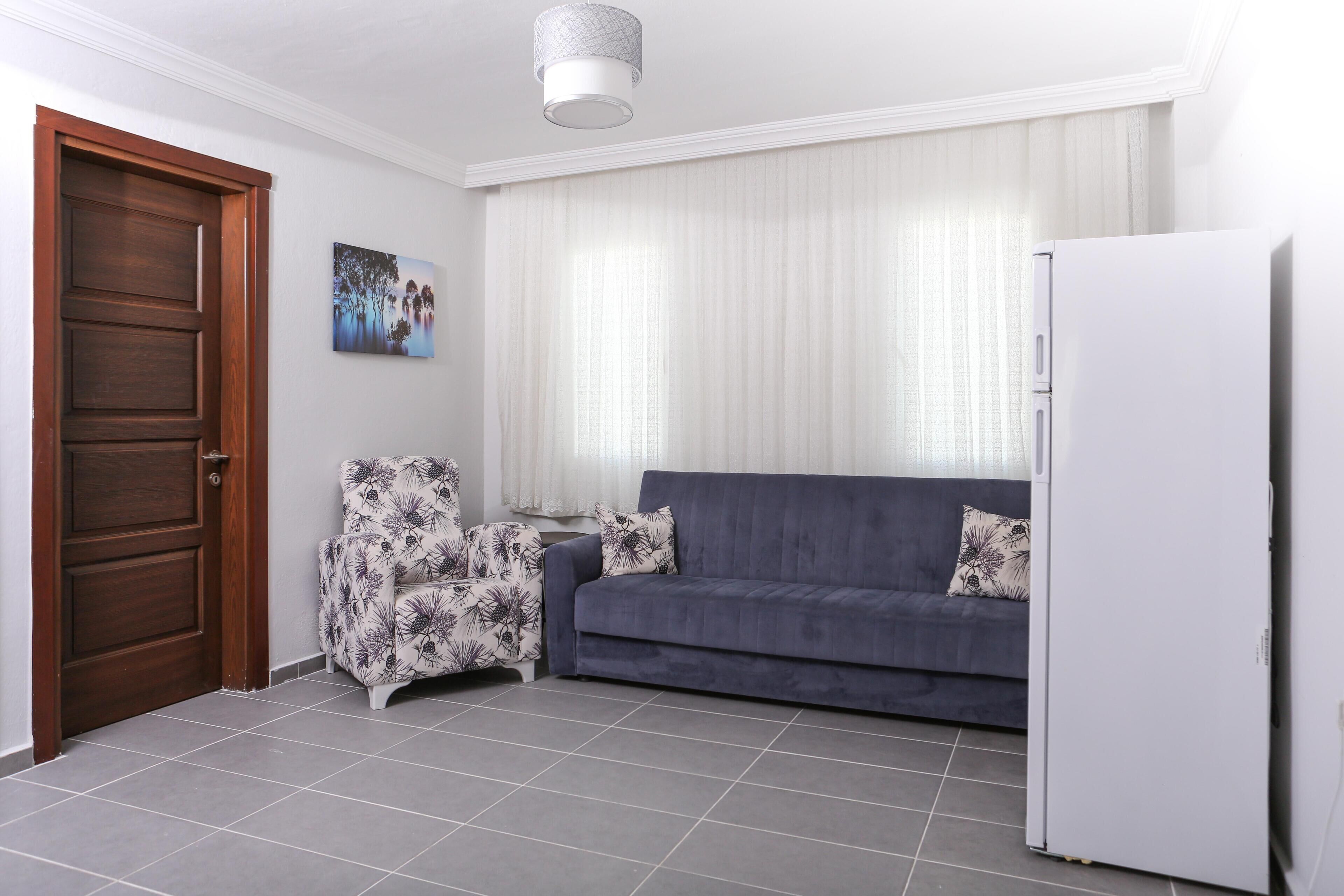 A living room with a dark blue sofa, a white refrigerator, a wooden door, and a patterned armchair.