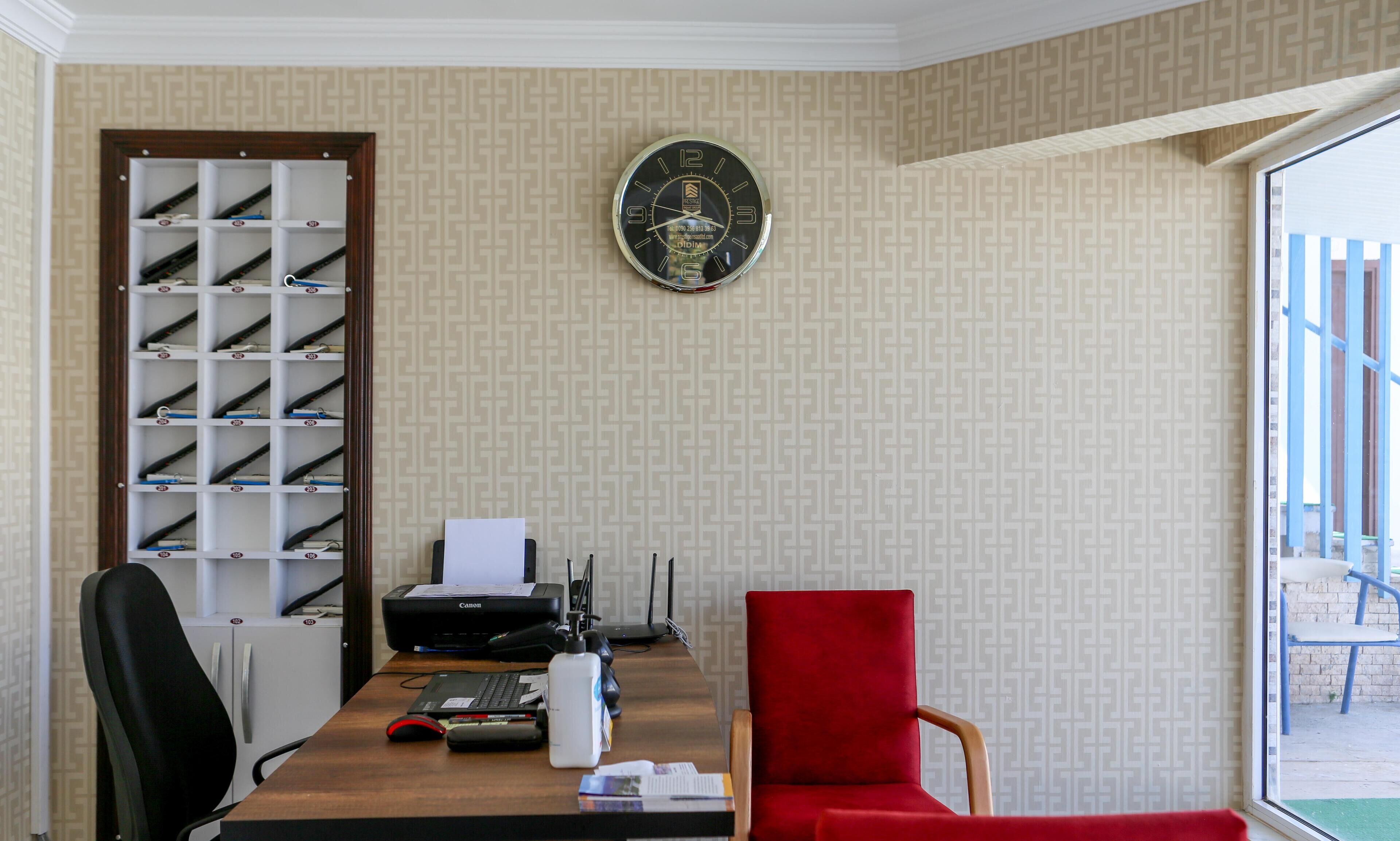 A hotel room with a wooden desk, a red chair, a Canon printer, and a wall clock.