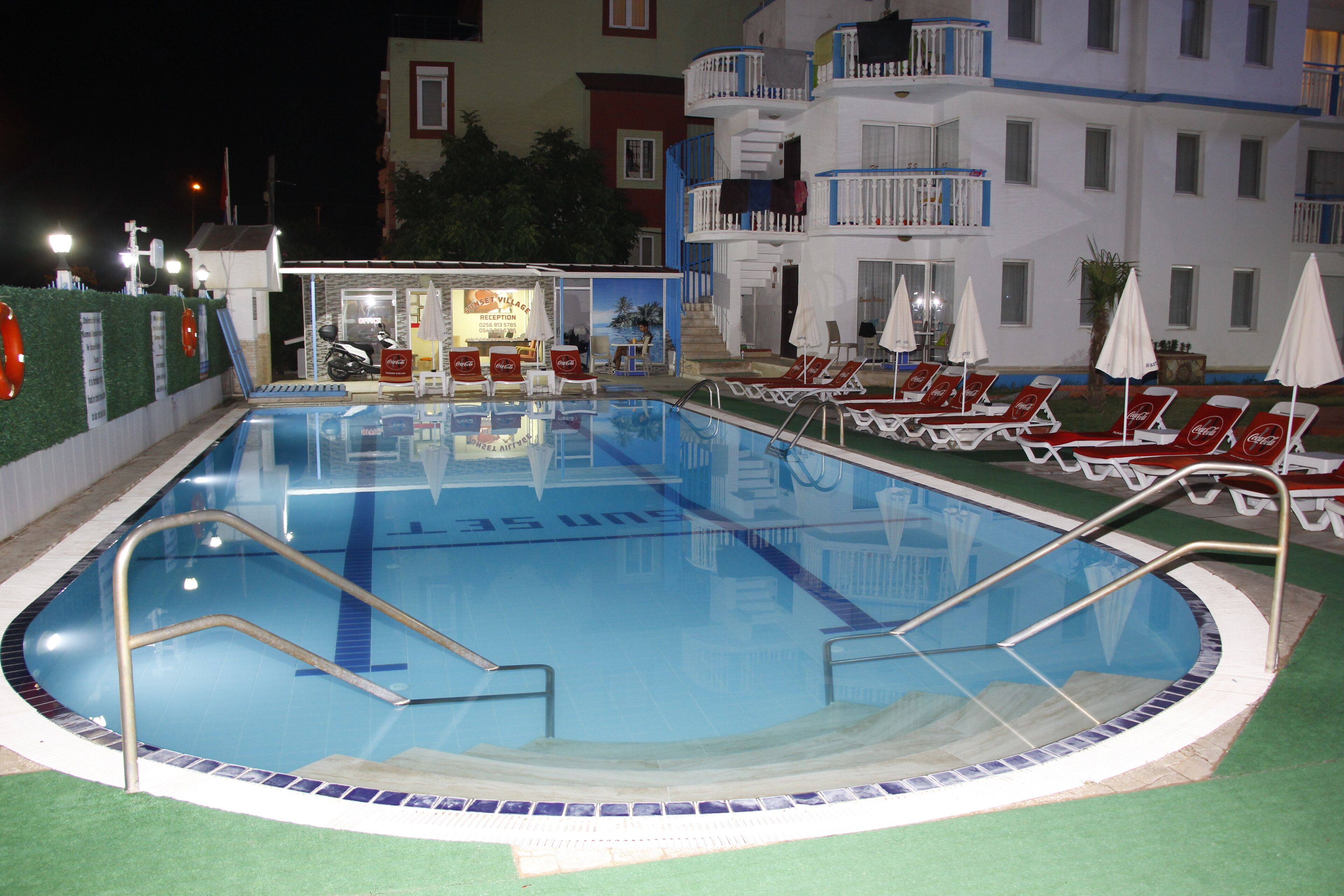 A swimming pool with lounge chairs and umbrellas, surrounded by a building with balconies.