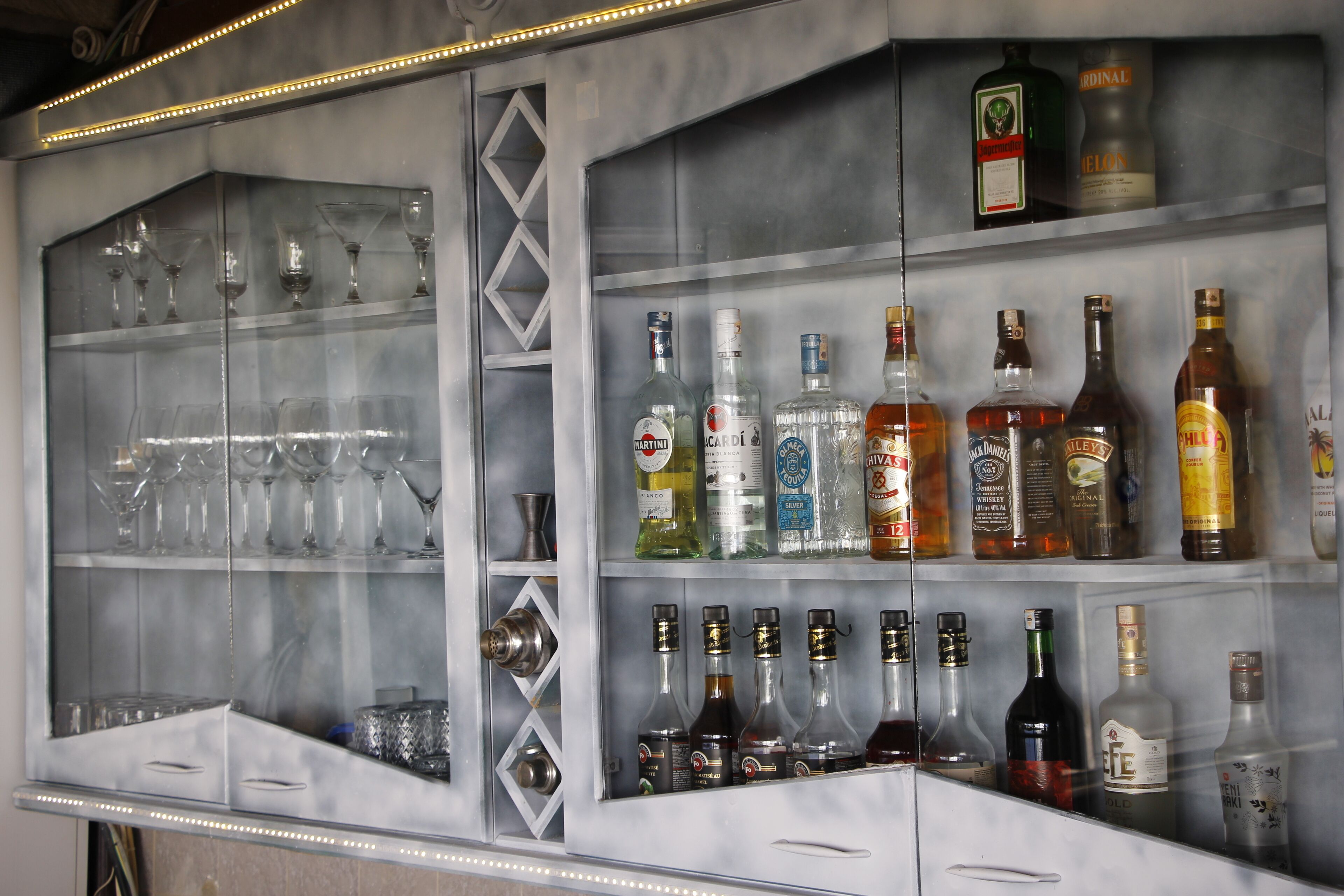 Un espace bar avec des étagères remplies de bouteilles d’alcool et de verres à vin vides.