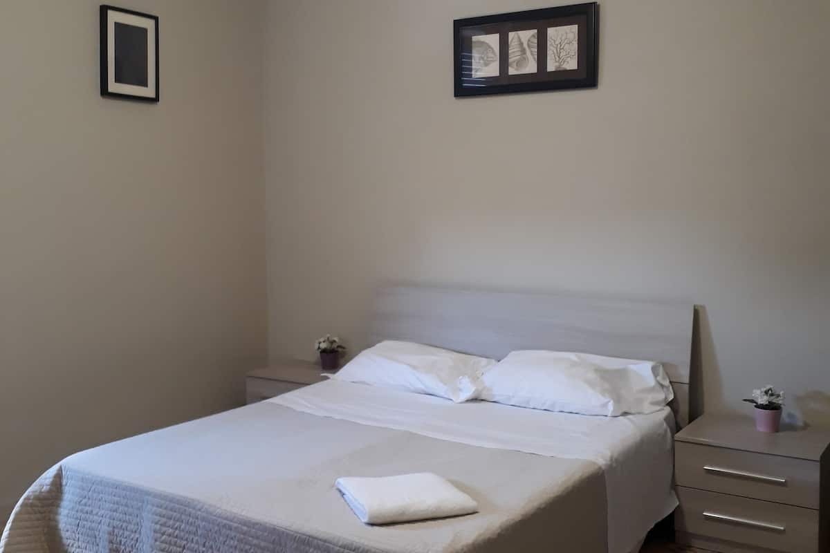 A neatly made bed with white linens, a ceiling fan, and a small bedside table with a plant.