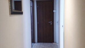 A narrow hallway with a wooden door at the end, a mirror on the left wall, and a light switch on the right wall. - 48 airport budget rooms (Pisa)