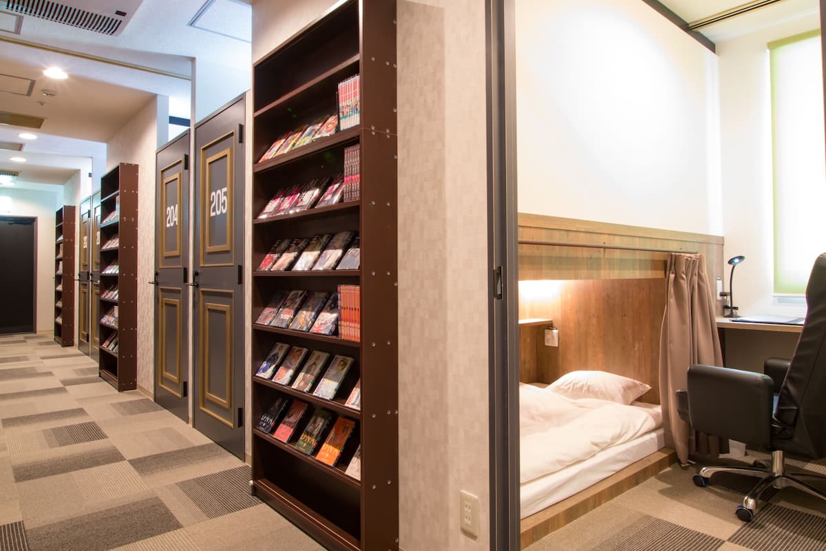 A hotel room with a bed, a desk, and a bookshelf containing books.