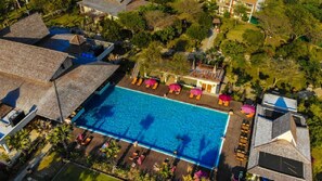 Luftaufnahme eines Resorts mit einem zentralen Swimmingpool, umgeben von Liegebereichen und Sonnenschirmen.