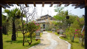 Un sentier mène à un bâtiment traditionnel, entouré d’une végétation luxuriante et de plantes en pot.