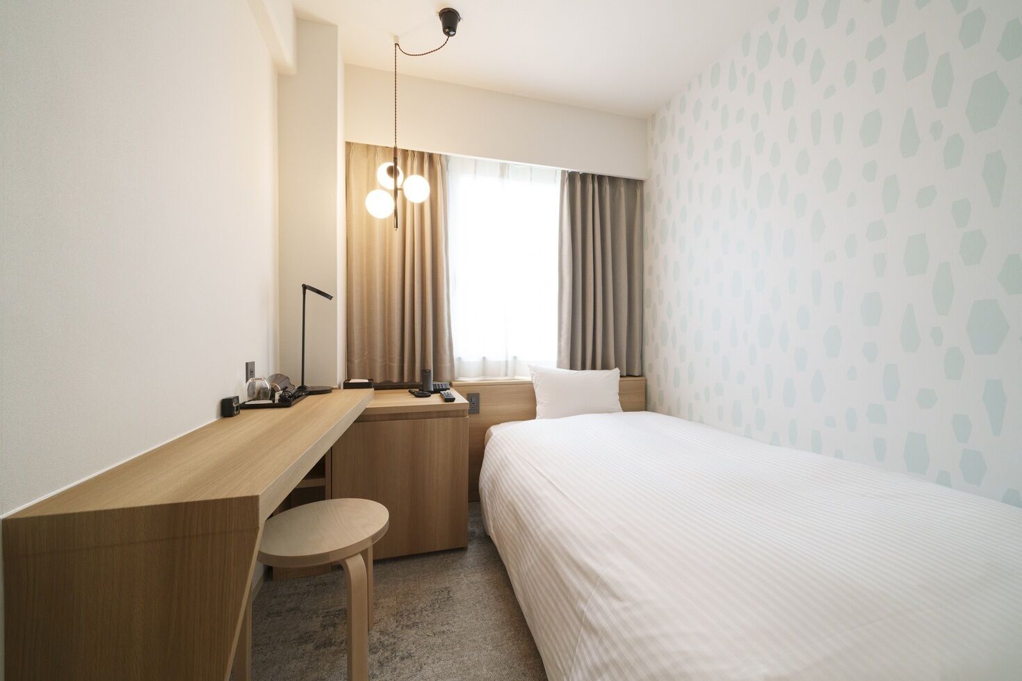 Hotellihuone, jossa on sänky, työpöytä, tuoli, lamppu ja ikkuna, jossa on verhot.