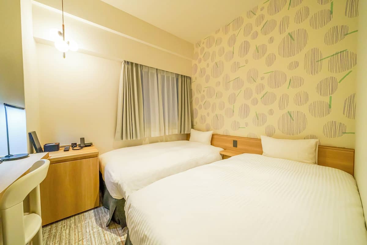 A hotel room with two beds, a desk, and a computer.