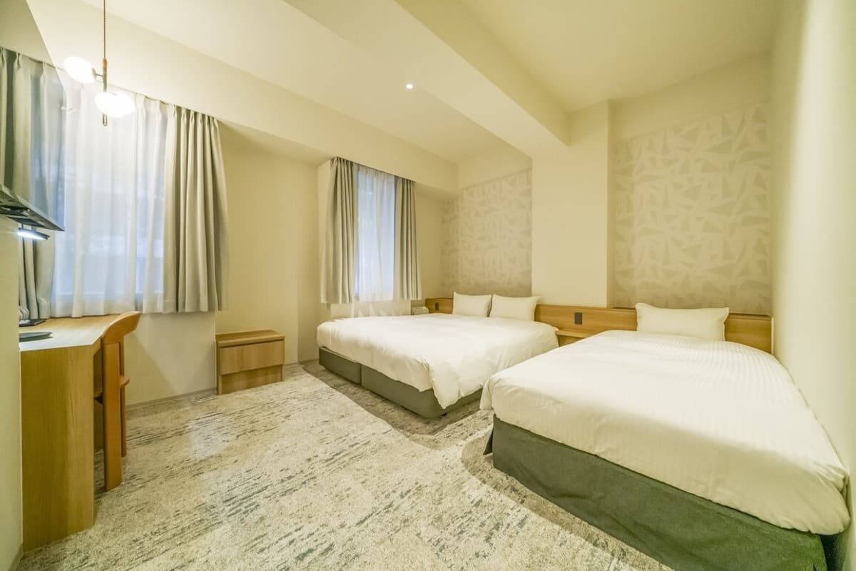 A hotel room with two beds, a desk, a chair, and a carpeted floor.