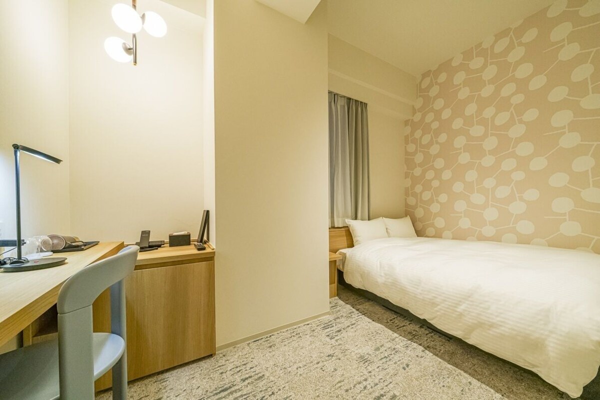 A hotel room with a bed, desk, chair, and a wall with a geometric pattern.