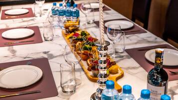 Una mesa de comedor dispuesta con platos, cubiertos, botellas de agua y un centro de mesa con velas.