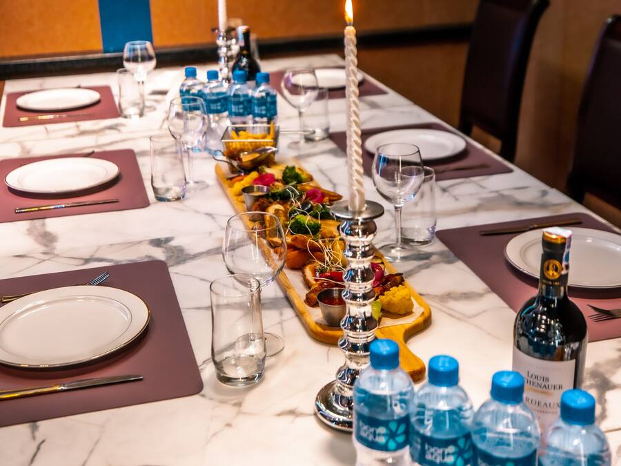 Una mesa de comedor dispuesta con platos, cubiertos, botellas de agua y un centro de mesa con velas.